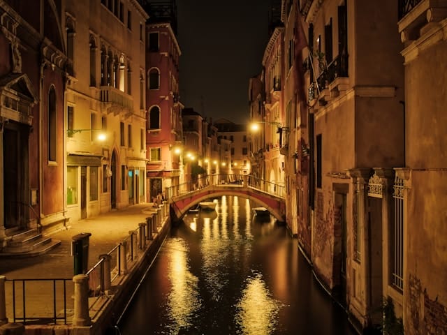 Canale veneziano di sera con ponte e palazzi illuminati